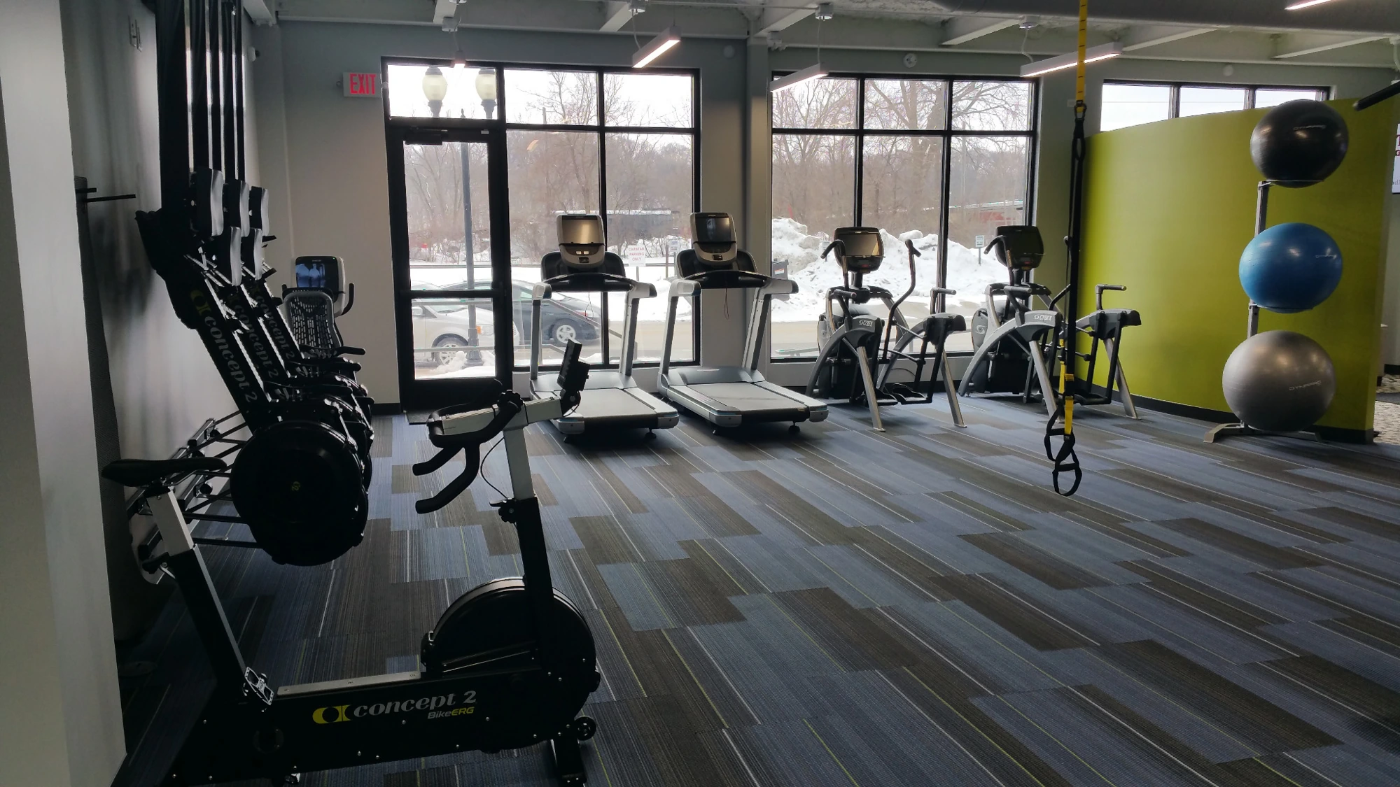 A turf training area with cardio and strength equipment near large windows.